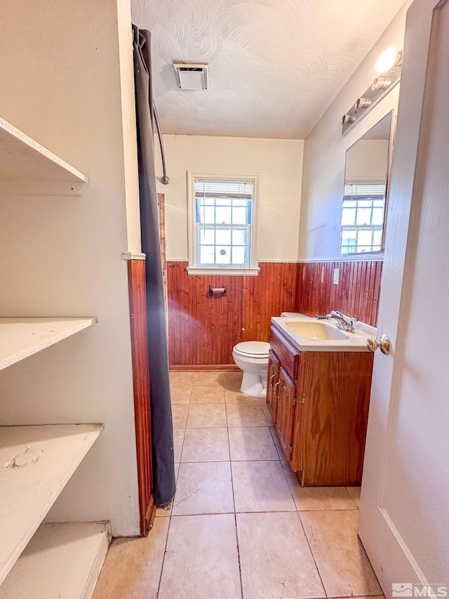 bathroom with wainscoting, toilet, wooden walls, vanity, and tile patterned flooring