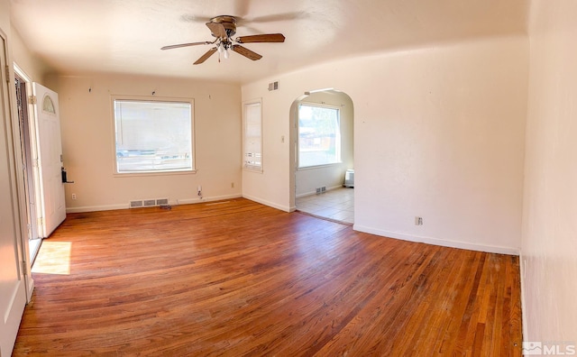 empty room featuring arched walkways, ceiling fan, light wood-style floors, and baseboards