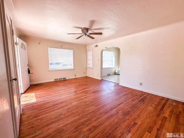 spare room with arched walkways, ceiling fan, wood finished floors, baseboards, and a textured ceiling