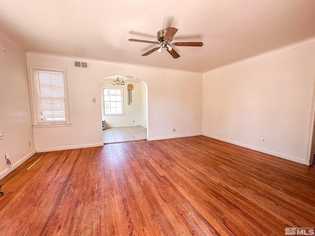 spare room with arched walkways, a ceiling fan, wood finished floors, and baseboards