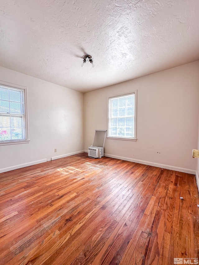 spare room with hardwood / wood-style floors, plenty of natural light, a textured ceiling, and baseboards