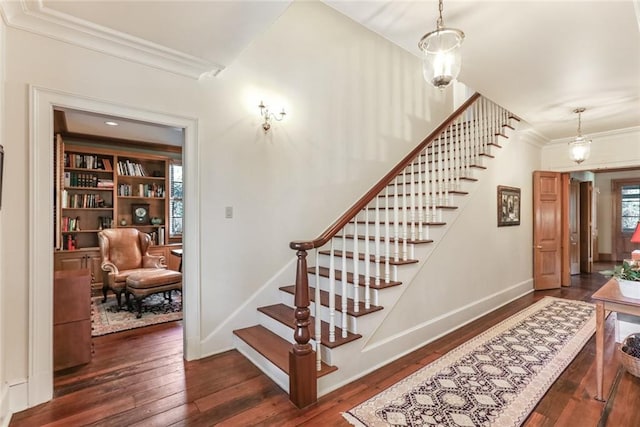 stairs with dark hardwood / wood-style flooring, an inviting chandelier, ornamental molding, and built in shelves