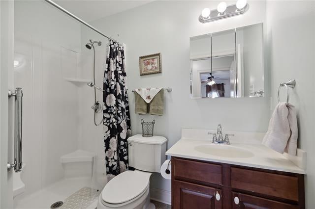 bathroom with ceiling fan, walk in shower, toilet, and vanity with extensive cabinet space