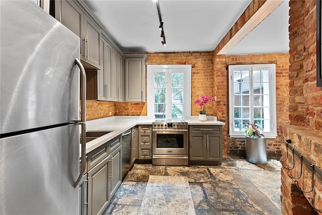 kitchen featuring brick wall, rail lighting, gray cabinets, and stainless steel appliances