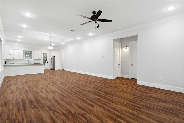 unfurnished living room with ceiling fan with notable chandelier, crown molding, and dark wood-type flooring