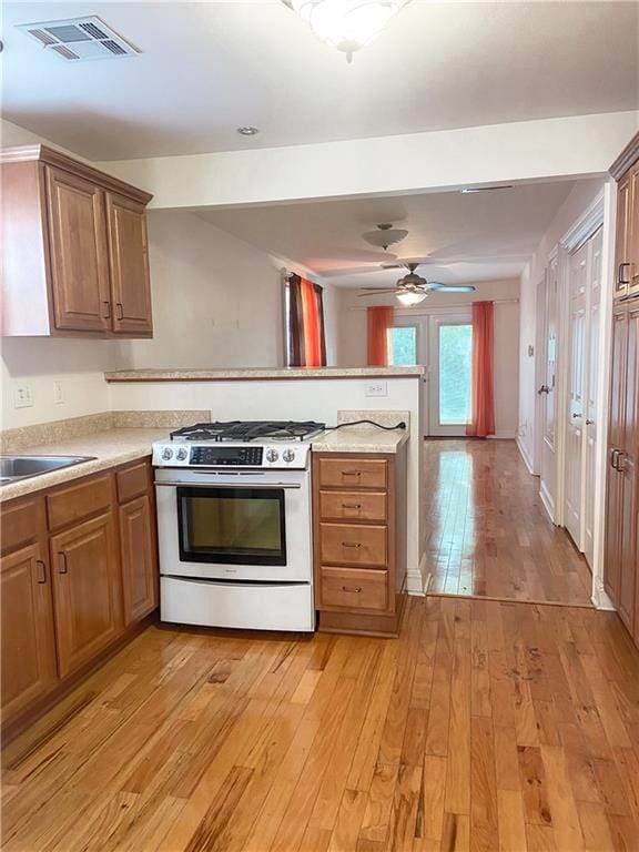 kitchen featuring kitchen peninsula, sink, ceiling fan, range with gas cooktop, and light wood-type flooring