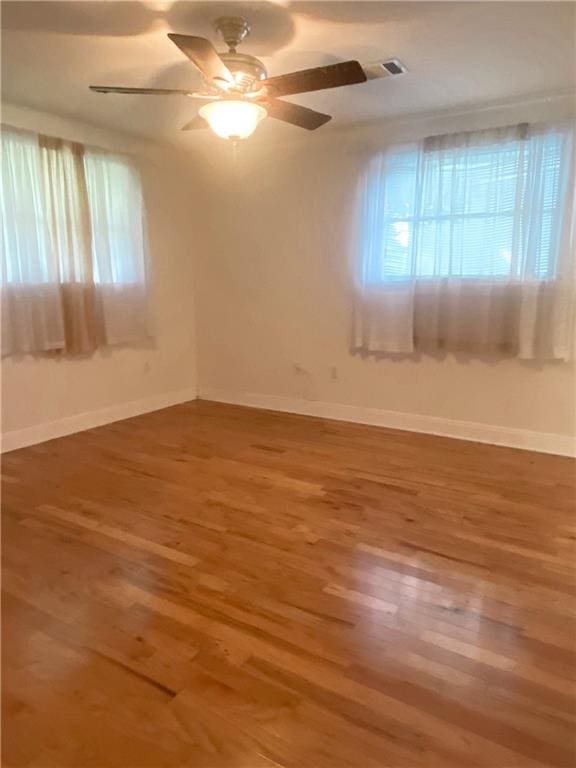 empty room featuring plenty of natural light, ceiling fan, and hardwood / wood-style flooring