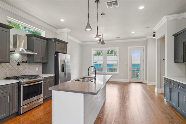 kitchen featuring decorative light fixtures, sink, light hardwood / wood-style flooring, stainless steel appliances, and wall chimney exhaust hood