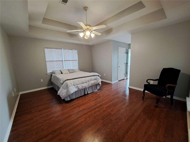 bedroom with dark hardwood / wood-style flooring, ceiling fan, and a tray ceiling