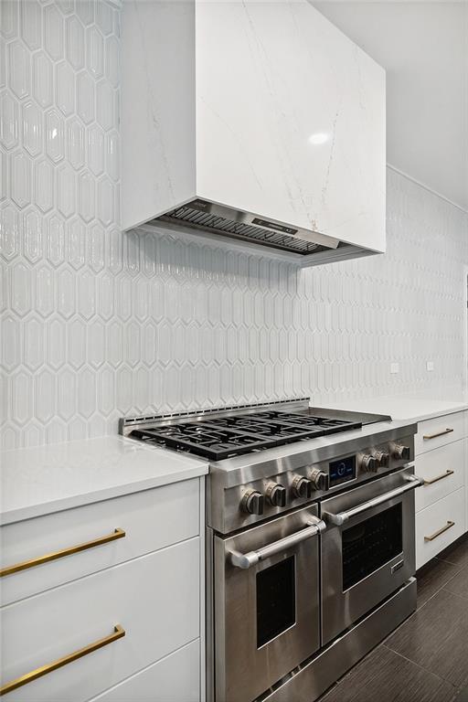 kitchen featuring tasteful backsplash, custom range hood, double oven range, and white cabinetry