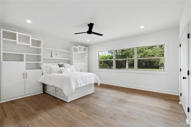 unfurnished bedroom featuring brick wall, multiple windows, light hardwood / wood-style floors, and ceiling fan