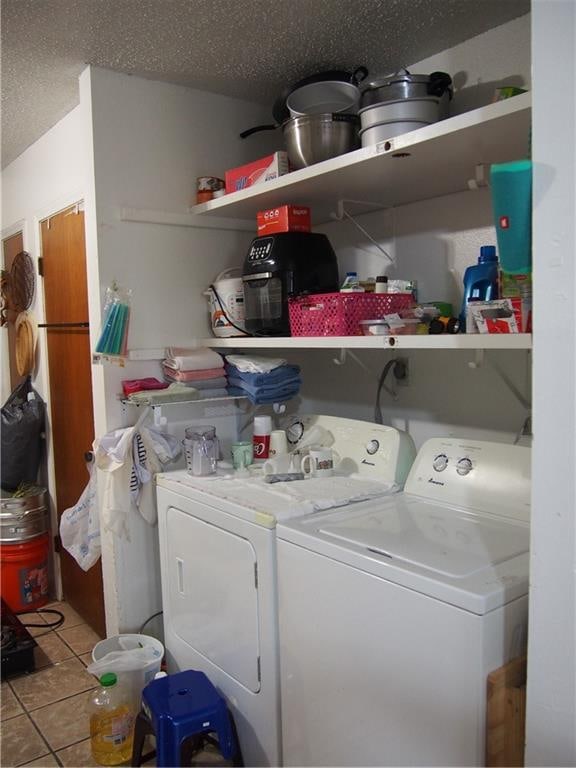 clothes washing area with a textured ceiling, separate washer and dryer, and light tile floors