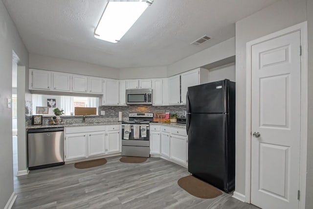 kitchen with light stone countertops, white cabinetry, light hardwood / wood-style floors, sink, and stainless steel appliances