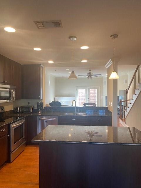 kitchen with stainless steel appliances, dark brown cabinetry, light hardwood / wood-style floors, and decorative light fixtures