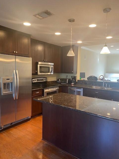 kitchen with light hardwood / wood-style flooring, stainless steel appliances, dark stone counters, and decorative light fixtures