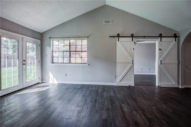 spare room with dark wood-type flooring, lofted ceiling, a textured ceiling, a barn door, and french doors