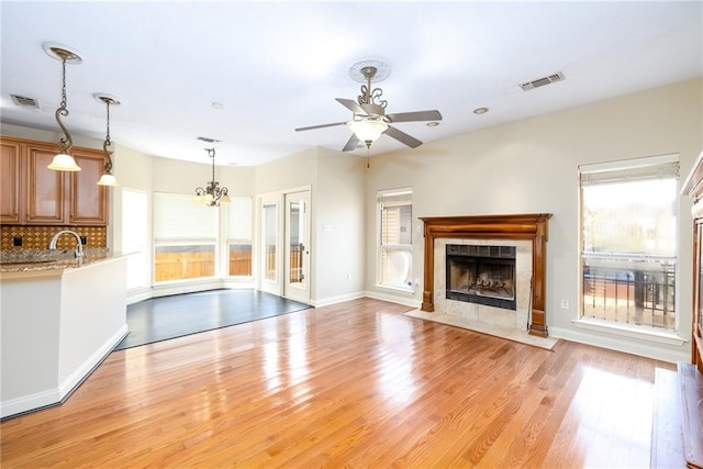 unfurnished living room featuring ceiling fan with notable chandelier, sink, a tile fireplace, and light hardwood / wood-style flooring