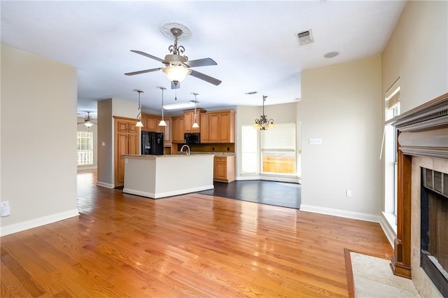 unfurnished living room with a wealth of natural light, a tile fireplace, light wood-type flooring, and ceiling fan with notable chandelier