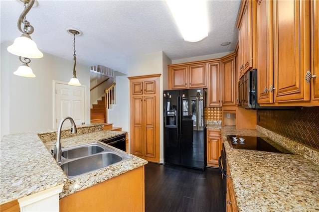 kitchen with decorative light fixtures, dark hardwood / wood-style flooring, light stone counters, black appliances, and sink