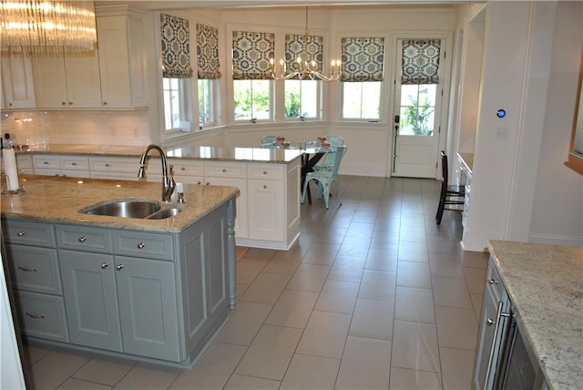 kitchen featuring light stone countertops, sink, an island with sink, and white cabinets