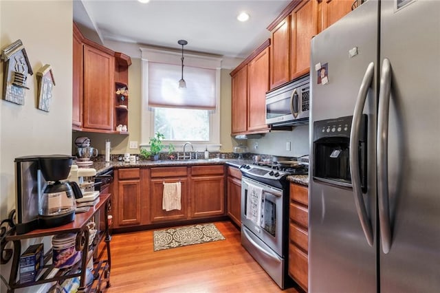 kitchen featuring hanging light fixtures, sink, light wood-type flooring, dark stone countertops, and stainless steel appliances