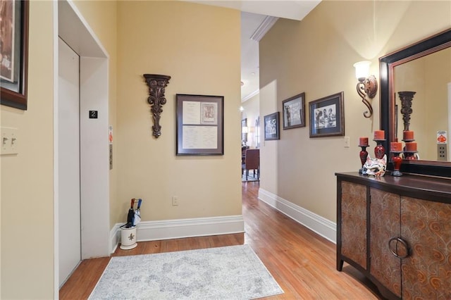 hallway featuring elevator, light wood-type flooring, and ornamental molding