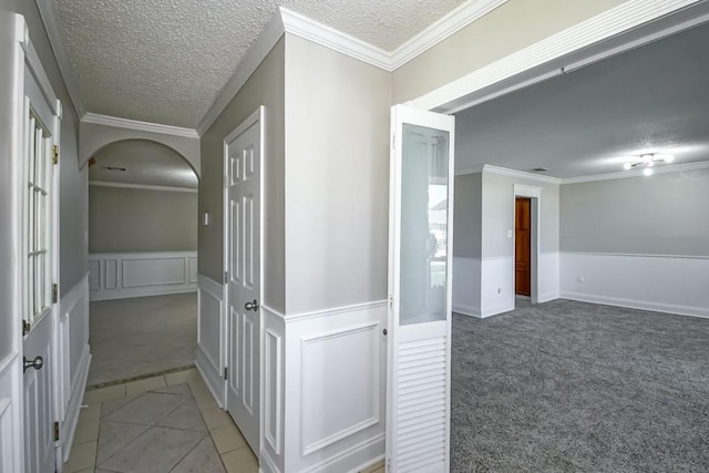 corridor with a wainscoted wall, crown molding, a textured ceiling, and light tile patterned flooring