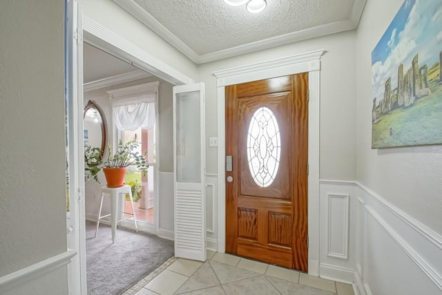 entrance foyer with a wainscoted wall, light tile patterned floors, light colored carpet, ornamental molding, and a textured ceiling