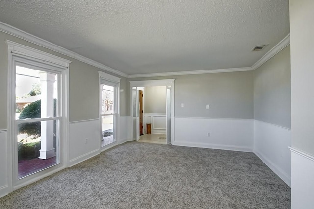 carpeted spare room with a wainscoted wall, a textured ceiling, visible vents, and crown molding