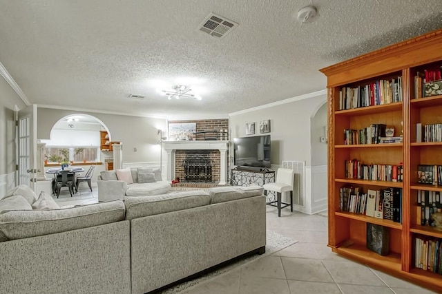 living room with arched walkways, light tile patterned flooring, visible vents, ornamental molding, and wainscoting