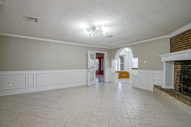 empty room featuring visible vents, arched walkways, a textured ceiling, a fireplace, and light tile patterned flooring