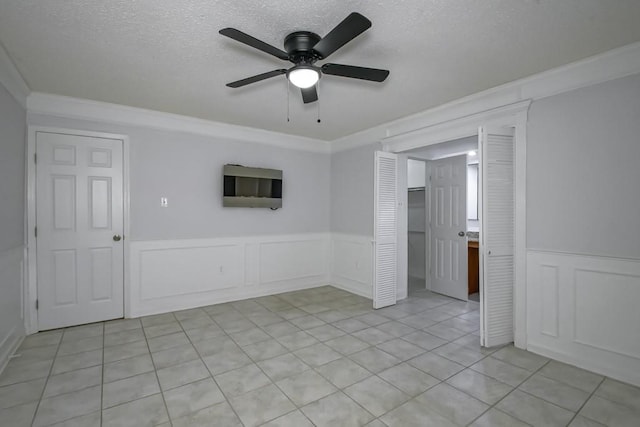 empty room featuring a textured ceiling, ornamental molding, a wainscoted wall, and light tile patterned flooring