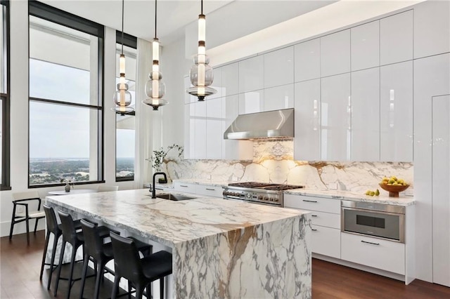 kitchen with pendant lighting, white cabinetry, sink, a kitchen island with sink, and exhaust hood