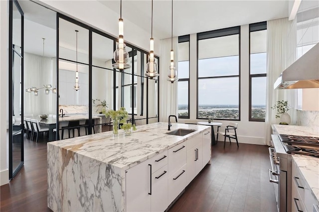 kitchen with white cabinetry, sink, high end range, light stone counters, and a center island with sink