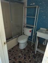 bathroom featuring toilet and bath / shower combo with glass door