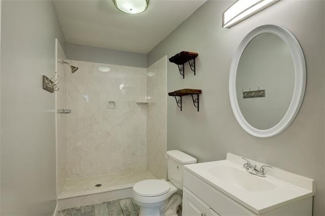 bathroom with toilet, a tile shower, and vanity