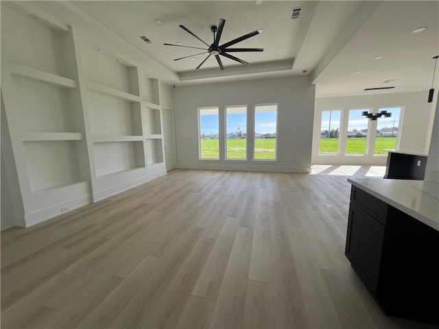 unfurnished living room featuring ceiling fan with notable chandelier, light hardwood / wood-style floors, and built in features