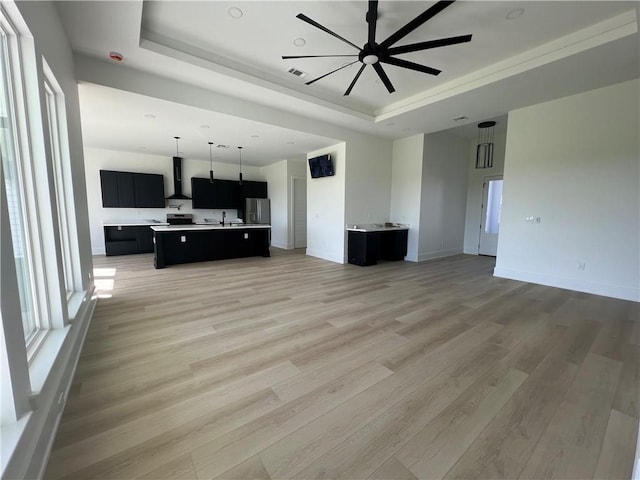 unfurnished living room with ceiling fan, a raised ceiling, light wood-type flooring, and sink