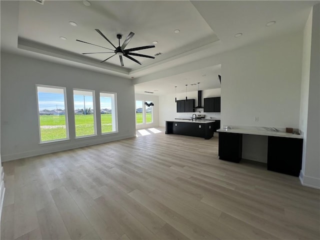 unfurnished living room with light hardwood / wood-style floors, a tray ceiling, and a healthy amount of sunlight