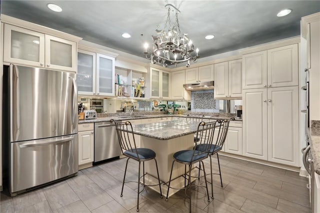 kitchen with appliances with stainless steel finishes, a kitchen island, light stone counters, and hanging light fixtures