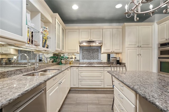 kitchen featuring light stone counters, sink, a chandelier, stainless steel appliances, and decorative backsplash