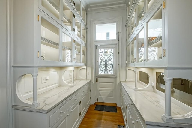 interior space with hardwood / wood-style flooring, crown molding, light stone counters, and white cabinets