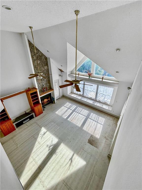 living room featuring a textured ceiling, ceiling fan, a fireplace, and high vaulted ceiling