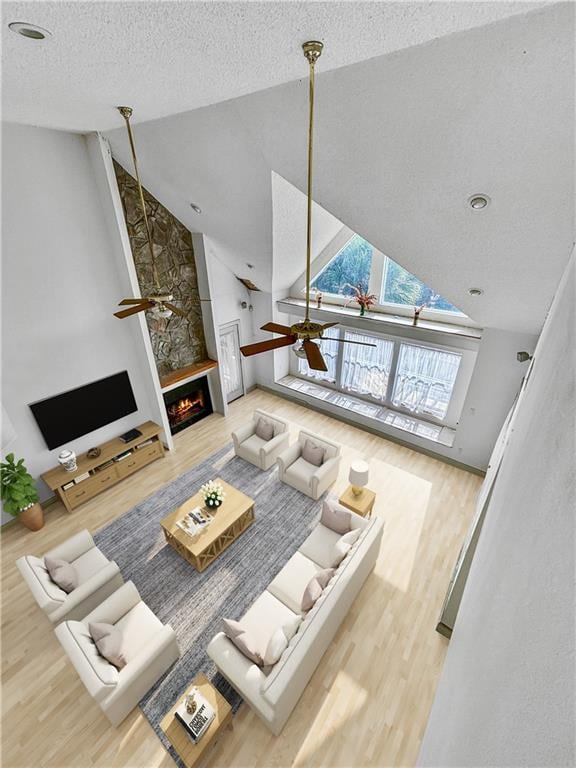 living room with high vaulted ceiling, hardwood / wood-style flooring, ceiling fan, a fireplace, and a textured ceiling