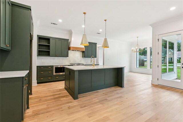 kitchen featuring custom exhaust hood, hanging light fixtures, a kitchen island with sink, sink, and ornamental molding