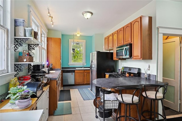 kitchen with track lighting, sink, stainless steel appliances, light tile floors, and a breakfast bar area