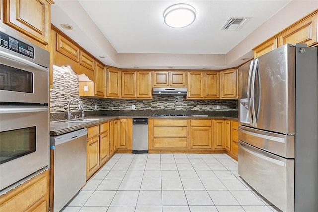 kitchen featuring tasteful backsplash, dark stone countertops, stainless steel appliances, sink, and light tile flooring