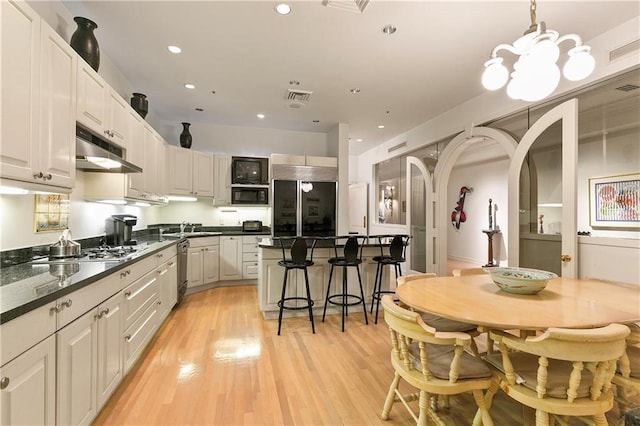 kitchen with sink, white cabinetry, light hardwood / wood-style flooring, built in appliances, and decorative light fixtures