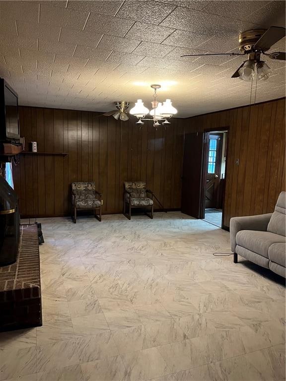 living area featuring a textured ceiling, wooden walls, and ceiling fan with notable chandelier