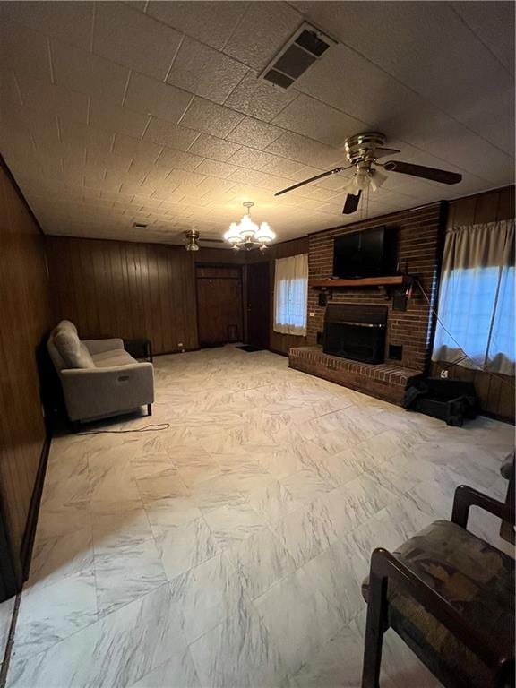 living room with a fireplace, ceiling fan with notable chandelier, and wooden walls